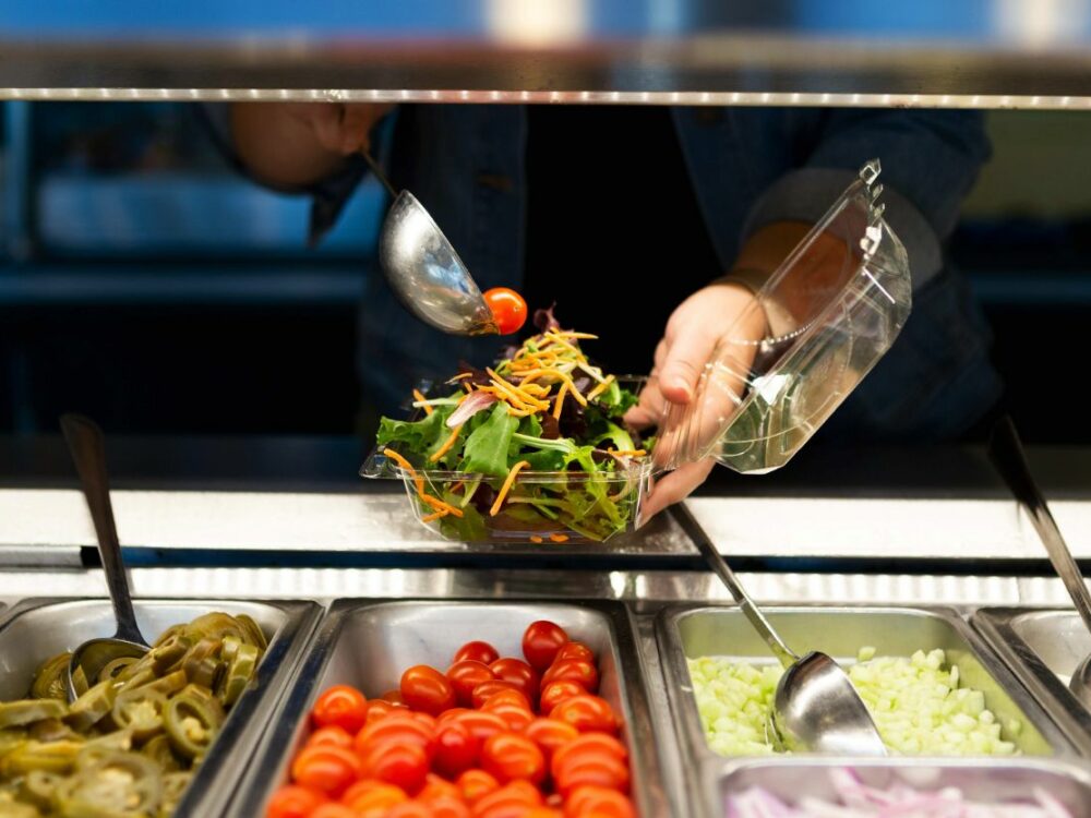 A person preparing a salad from the salad bar.