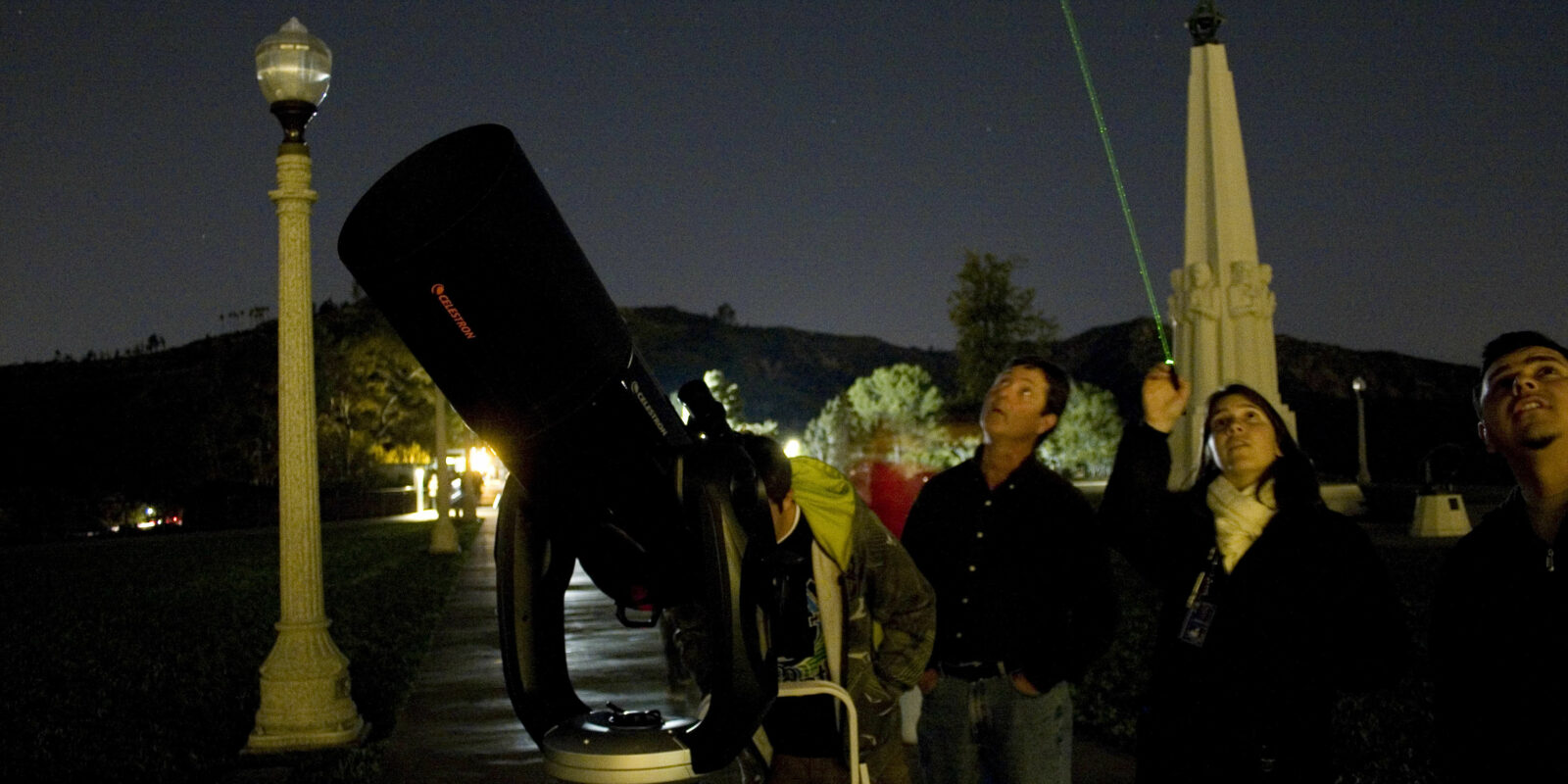Telescope demonstrator Katy Haugland uses a laser to point out celestial wonders to Observatory patrons while standing next to a telescope on the lawn.